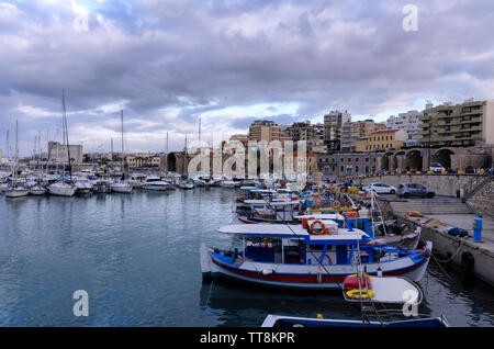 Heraklion, Crete - Greece. View to the old Venetian port with the traditional fishing boats and the Heraklion city with the old Venetian shipyards Stock Photo