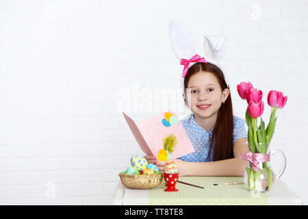 Cute girl with greeting card and decorated Easter eggs, on light background Stock Photo