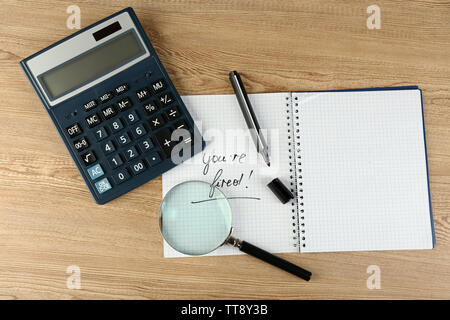 Message You're Fired on notebook with calculator, marker and magnifying glass on wooden table, closeup Stock Photo