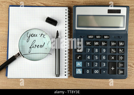 Message You're Fired on notebook with calculator, marker and magnifying glass on wooden table, closeup Stock Photo