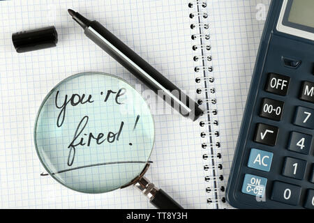 Message You're Fired on notebook with calculator, marker and magnifying glass on wooden table, closeup Stock Photo