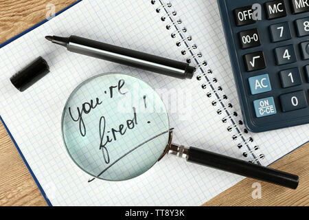 Message You're Fired on notebook with calculator, marker and magnifying glass on wooden table, closeup Stock Photo