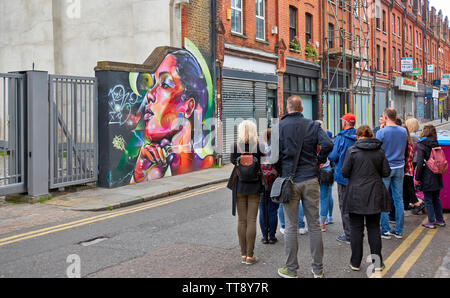 LONDON ENGLAND BRICK LANE GROUP OF PEOPLE STUDYING WALL ART IN THE AREA Stock Photo