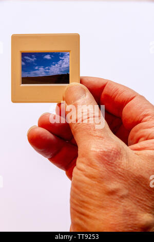 A man's hand holding up to the light a 35mm colour film slide of a landscape view Stock Photo