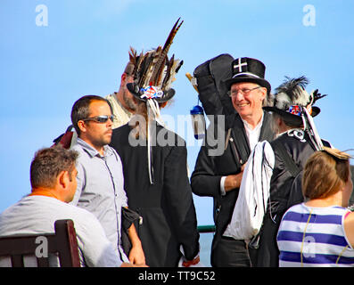 SIDMOUTH, DEVON, ENGLAND - AUGUST 5TH 2012: Three Morris dancers chat to passers by on the Esplanade. Stock Photo