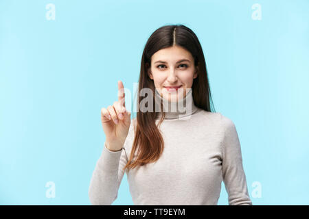 beautiful young caucasian woman pressing a virtual button, looking at camera smiling, isolated on blue background Stock Photo