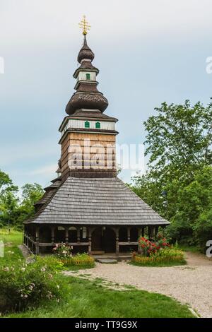 Prague, Czech Republic - June 14 2019: Church of the Archangel Michael from 18th century with shingled roof standing in Kinsky garden. Red roses bush. Stock Photo