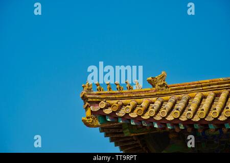 Gold traditional chinese roof against deep blue summer sky. A row of mythical creatures (including a dragon) are carved above the tiles Stock Photo
