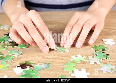 Female hands assembling puzzle on wooden table, closeup Stock Photo