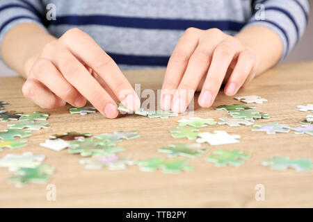 Female hands assembling puzzle on wooden table, closeup Stock Photo