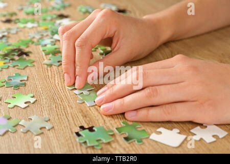 Female hands assembling puzzle on wooden table, closeup Stock Photo