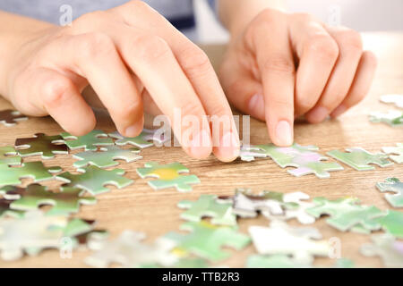 Female hands assembling puzzle on wooden table, closeup Stock Photo