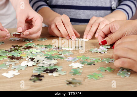 Female hands assembling puzzle on wooden table, closeup Stock Photo