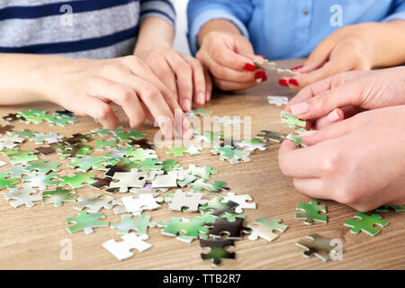 Female hands assembling puzzle on wooden table, closeup Stock Photo
