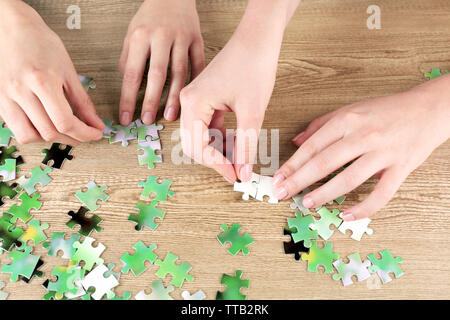 Female hands assembling puzzle on wooden table, closeup Stock Photo