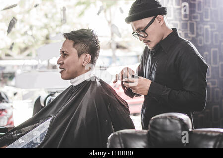 Portrait of barber hairstyle a costumer hair who sitting in chair with hand and pomade in barbershop or salon Stock Photo