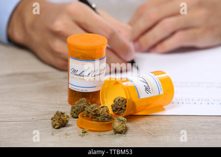 Doctor writing on prescription blank and bottle with medical cannabis on table close up Stock Photo