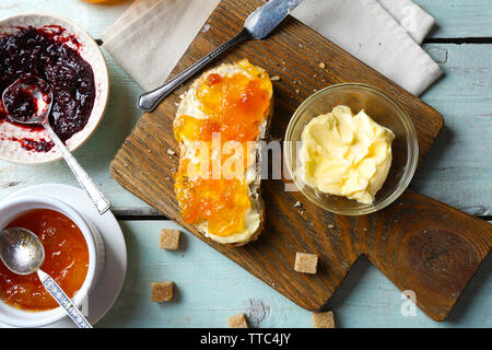 Tasty jam in the bowls, butter, fresh bread and tablet on blue wooden background Stock Photo