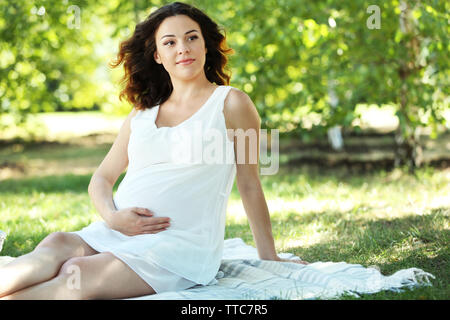Attractive pregnant woman on white blanket in the park Stock Photo