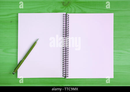 Blank page of an opened notebook with a green pen on green colored wooden table Stock Photo