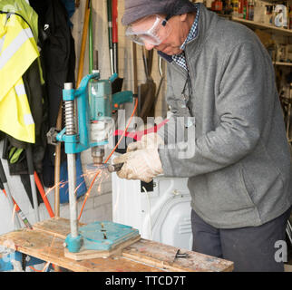 Man grinding burrs or mushroom head from the end of a cold chisel using an electric drill fitted with a grinding  wheel. Stock Photo