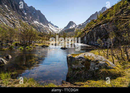 Beautiful wooded valley with stream surrounded by high peaks with snow in spring, Lofoten Islands, Norway, north of the arctic circle Stock Photo