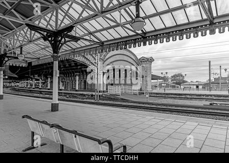 York Railway station where two19th Century canopies of iron and glass cover the platforms.  A bench is in the foreground and a cloudy sky is overhead. Stock Photo