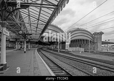 York Railway station where two19th Century canopies of iron and glass cover the platforms.  The platform curves into the station and a cloudy sky is a Stock Photo