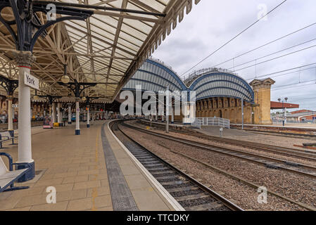 York Railway station where two19th Century canopies of iron and glass cover the platforms.  The platform curves into the station and a cloudy sky is a Stock Photo