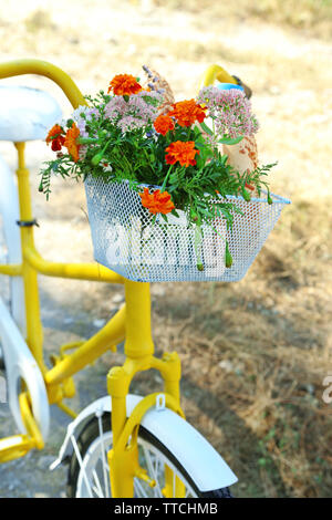 Beautiful yellow bicycle with bouquet of flowers, milk bottle and bread in basket, outdoors Stock Photo