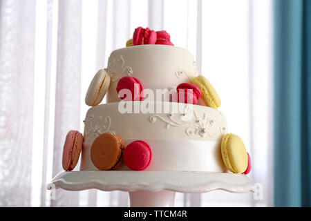 Beautiful wedding cake decorated with flowers on pink table in the room Stock Photo