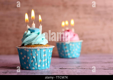 Tasty cupcakes with candles on violet table against wooden background Stock Photo