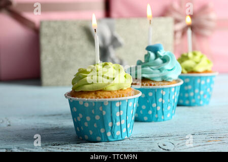 Delicious cupcakes with candles on violet table against wooden background Stock Photo