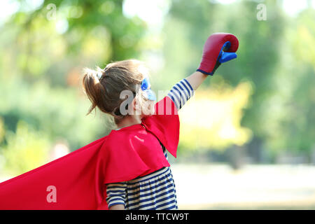 Cute little girl dressed as superhero in boxing gloves at the park Stock Photo
