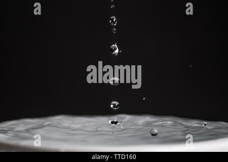 Close up macro photography of a  water drop splashing into water with a dark colored black gray background Stock Photo