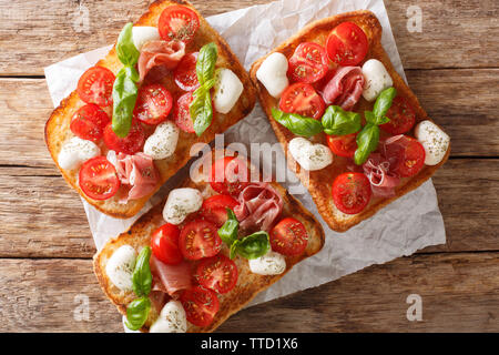 Italian open sandwiches with mozzarella, tomatoes, ham and basil closeup on the table. Horizontal top view from above Stock Photo