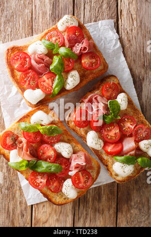 Italian open sandwiches with mozzarella, tomatoes, ham and basil closeup on the table. Vertical top view from above Stock Photo