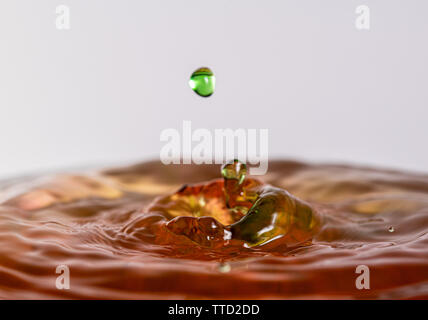 Close up macro photography of a red and green water drop splashing into water with a light colored white gray background Stock Photo