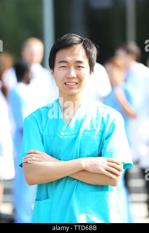 Young smiling doctor standing against group of medical workers Stock Photo