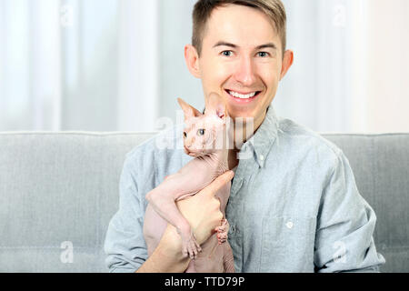 Young handsome man sitting with cat on couch at home Stock Photo