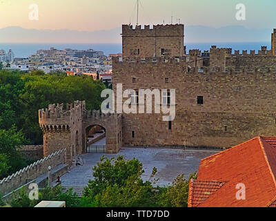 Castle gate and fortifications in Rhodes island old town Greece, at sunset time, trees and residential buildings.