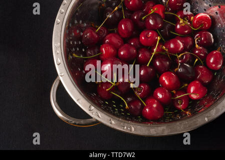 Fresh red cherries in metal colander on dark background, top view Stock Photo