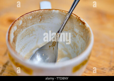 Empty cappuccino cup with a silver colored spoon is standing on a wooden table Stock Photo