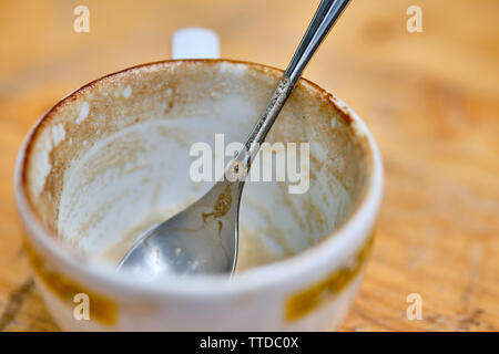 Empty cappuccino cup with a silver colored spoon is standing on a wooden table Stock Photo