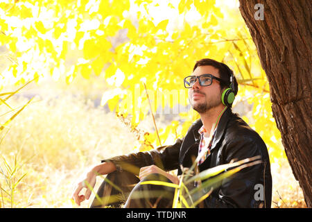 Young man sitting under the tree and listening to music Stock Photo