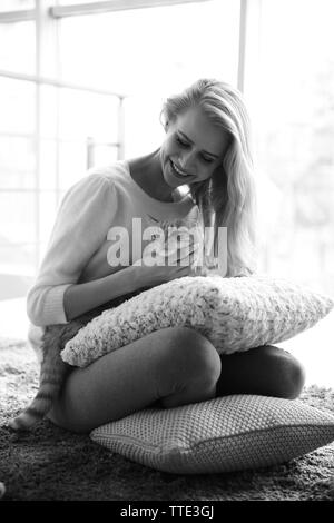 Black-and-white photo of attractive young woman playing with red cat on the floor Stock Photo