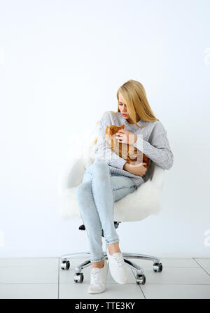 Young woman with red cat sitting on chair against white background Stock Photo