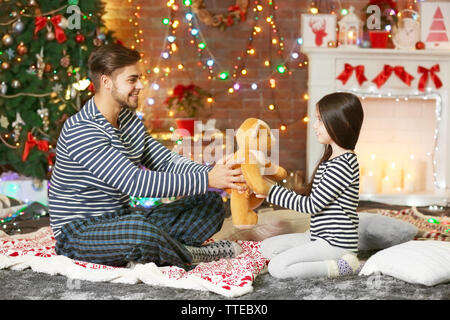 Older brother giving little sister a Teddy bear in Christmas living room Stock Photo