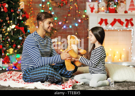 Older brother giving little sister a Teddy bear in Christmas living room Stock Photo