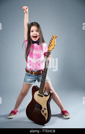 Beautiful artistic little girl playing guitar on grey background Stock Photo